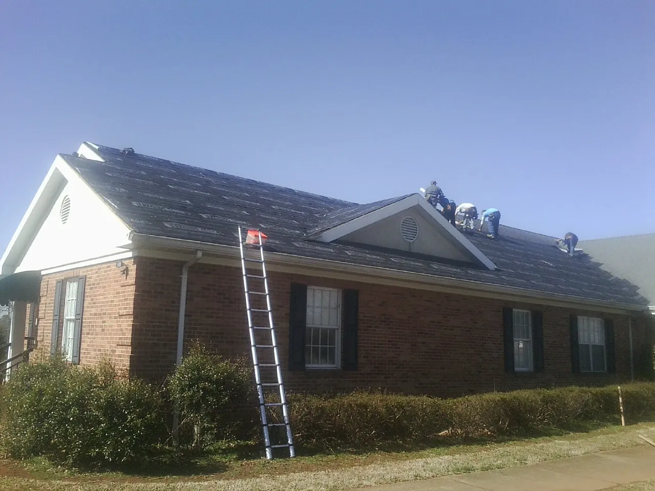 Crew tearing shingles off a brick ranch roof with a ladder set — Metal Roof Repair work by our crew in Whiteford