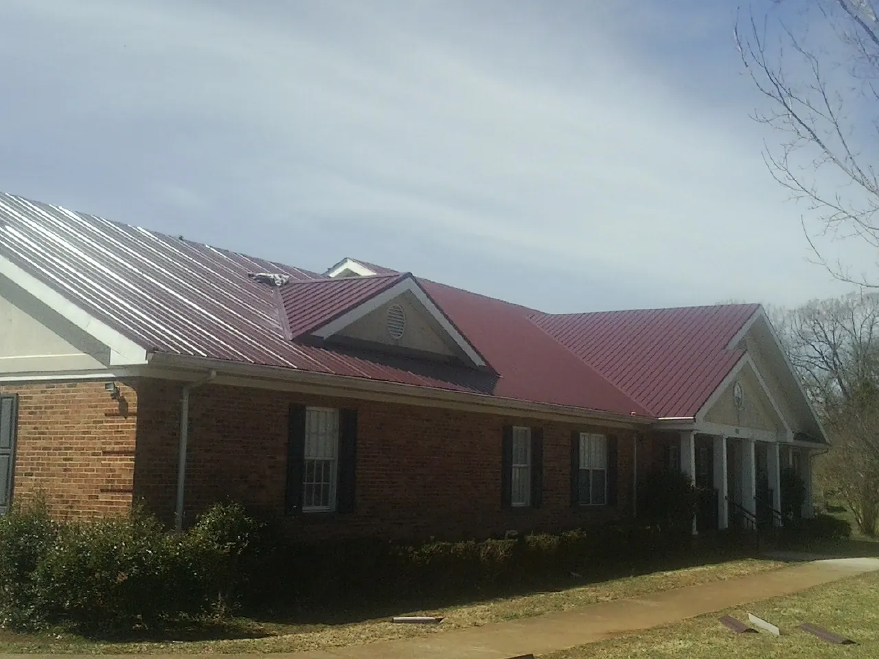 Red metal roof with gabled entries on a long brick building, from a Hail Damage Roof Repair job in Whiteford