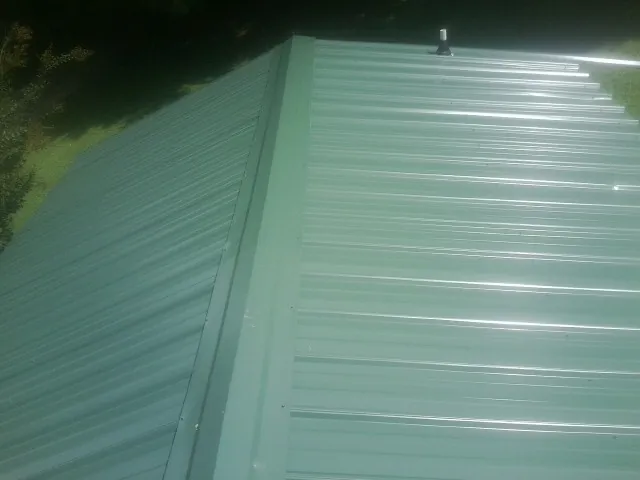 New green metal panels meeting at the ridge of a roof — Flat Roof Repair work by our crew in Whiteford