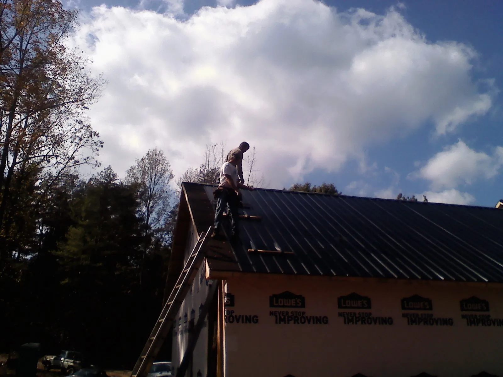 Roofer fastening dark metal panels high against a cloudy sky, from a Roof Inspection job in Whiteford
