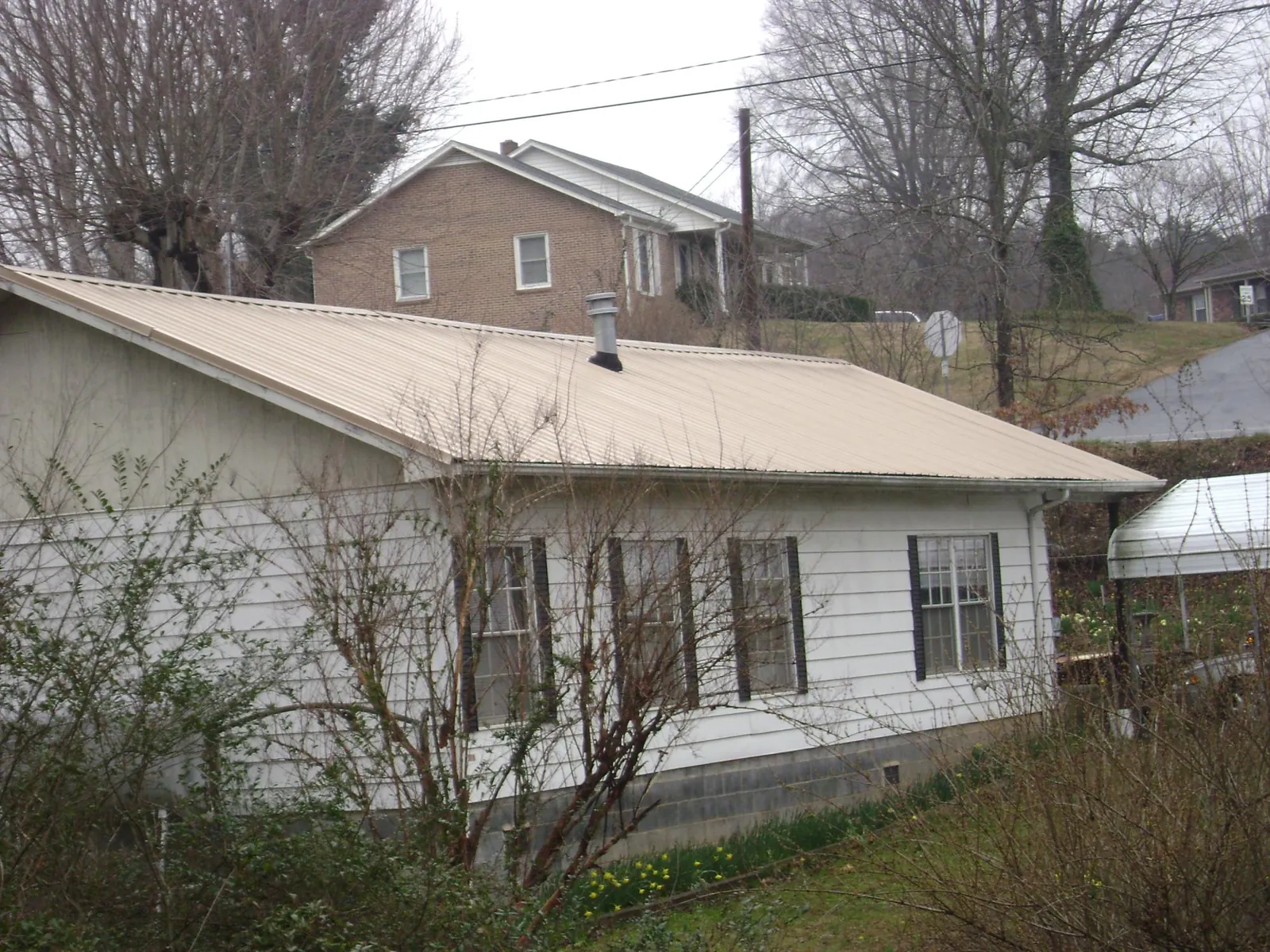 Tan metal roof on a white sided house set into a hillside — Commercial Roofing by Roofing Brothers in Whiteford